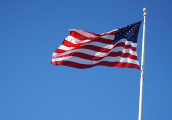    waving USA flag on pole against blue sky