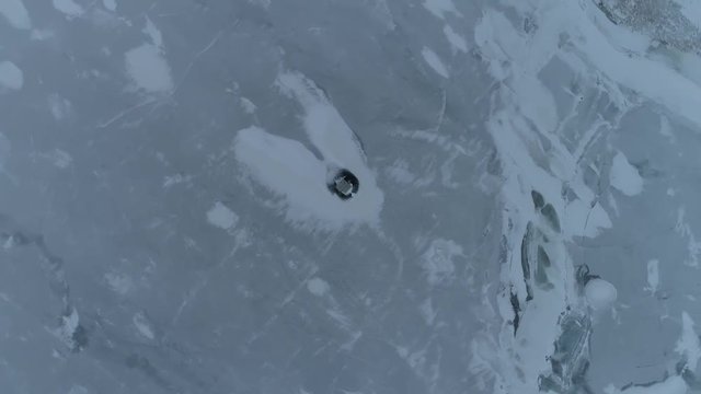 Spinning overhead drone shot raising up above ice fishing shack on a frozen lake.  Snow on the ice.  Slow spinning movement looking directly down.