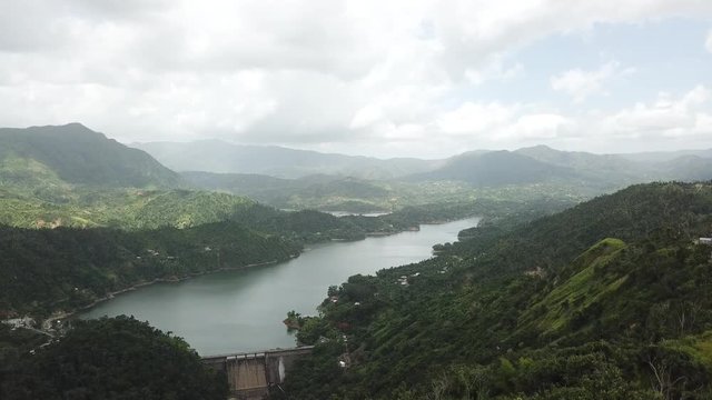 AERIAL: hiding the entire valley, containing a dam and a lake, behind a mango tree on the mountain tops of Utuado, Puerto Rico.