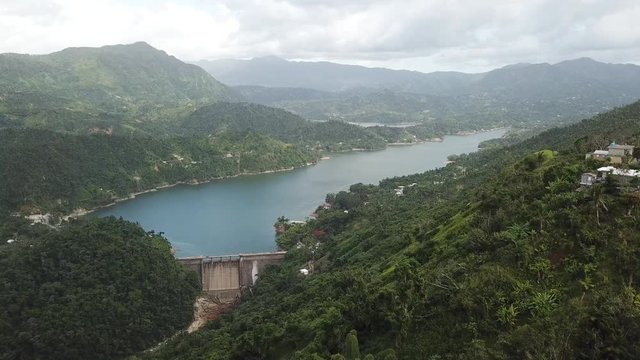 AERIAL: pushing down a mountain towards a dam and precious lake in the mountain tops of Utuado, Puerto Rico.