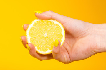 Hand with yellow painted nails holding a fresh lemon