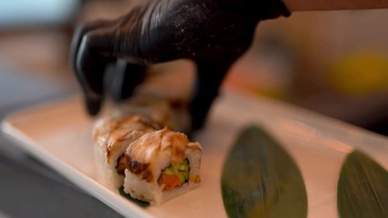 Close shot of susi rolls. Chef put more sushi on plate. Also there is 2  green leaves on the plate for decoration