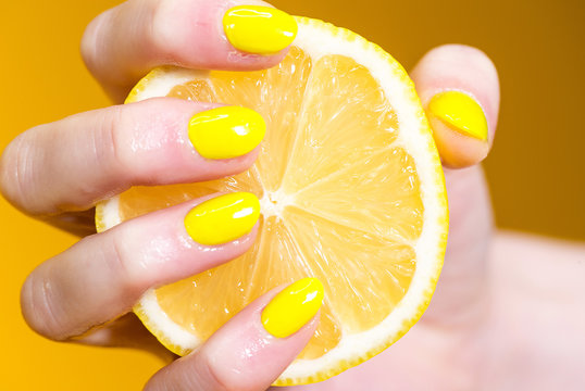 Hand with yellow painted nails holding a fresh lemon