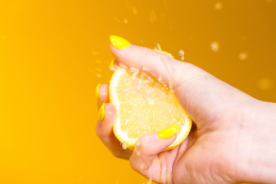 hand with yellow fingernails crushing a fresh, juicy lemon