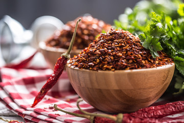 Dried and crushed chili peppers in wooden bowles with parsley herbs