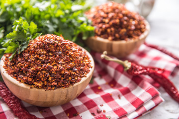 Dried and crushed chili peppers in wooden bowles with parsley herbs