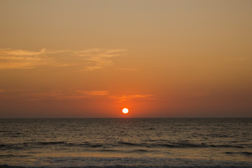 orange sun in a purple gray pink sunset sky against the background of the ocean