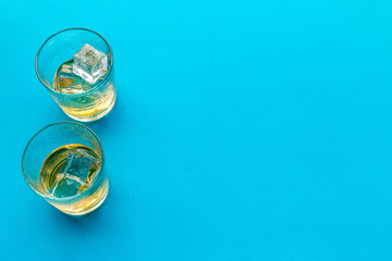 Glass of whiskey with ice on blue background top view copy space