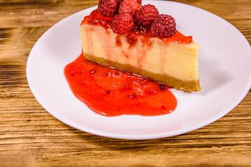 White plate with cheesecake New York and raspberries on wooden table