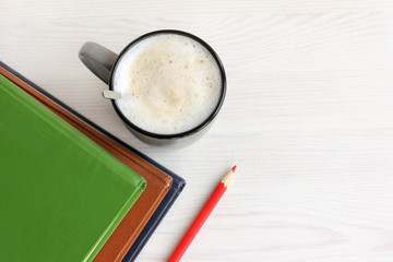 smart breakfast. mug with frothy cappuccino and three books with red pencil top view