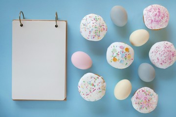 Easter food. Easter eggs in  pastel colors and sweet Easter pastries with an empty notebook on a light blue pastel background.copy space.top view