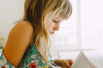 Fototapeta premium Little girl reading a book in a well lit bedroom