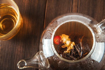 A cup of tea with fresh leaves of green and black tea on a textural dark wooden background with copy space. Flower tea in a glass teapot and steam