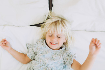 Cute little girl resting with closed eyes and smiling on a bed at home. Leisure. Family concept..