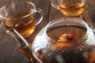 A cup of tea with fresh leaves of green and black tea on a textural dark wooden background with copy space. Flower tea in a glass teapot and steam