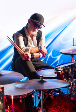 Drummer with drum sticks sitting in front of a drum set on stage