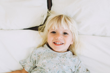 Cute little girl resting and smiling on a bed at home. Leisure. Family concept..