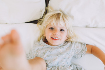 Cute little girl resting and smiling on a bed at home. Leisure. Family concept..