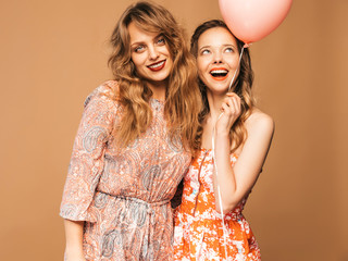 Two smiling beautiful women in summer hipster dresses. Girls posing on golden background.Models with colorful air balloons.Having fun, ready for celebration birthday or holiday party