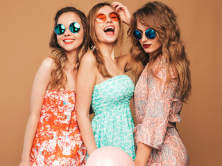 Three smiling beautiful women in summer hipster dresses. Girls posing on golden background.Models with colorful air balloons.Having fun, ready for celebration birthday or holiday party