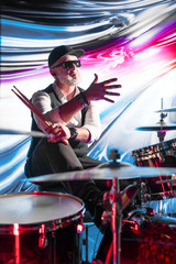 Emotional drummer playing on drum set on stage in the color light