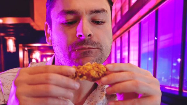 Young man eating tasty grilled chicken wing interior background with Cool Neon Lights like purple, blue, and pink duotone gradients, Crispy fried chicken