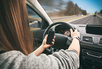 Young woman driving the car and looking on her phone