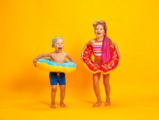 happy children girl and boy in swimsuit with swimming ring donut on colored yellow background.