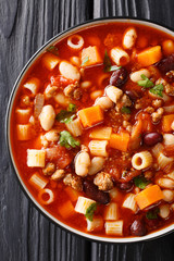 Thick Italian Pasta fagioli soup close-up in a bowl on the table. Vertical top view from above