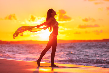 Sexy woman silhouette feminine curves bikini body swimsuit lady with scarf flying in the wind at sunset glow flare for weight loss sensuality concept. Sun vacation travel beach. - Powered by Adobe