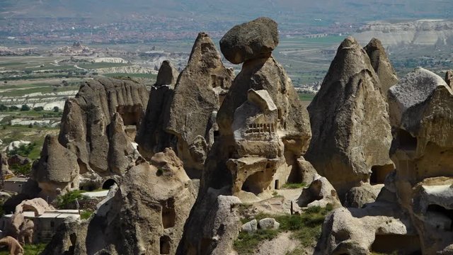 Wide shot of a collection of steep rock chimneys and cave entrances and countryside in the background