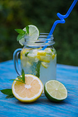 Citrus lemonade with mint in glass of citrus around on wooden table on blue background