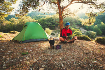 Traveler relaxes in the mountains among lush pines next to a burner