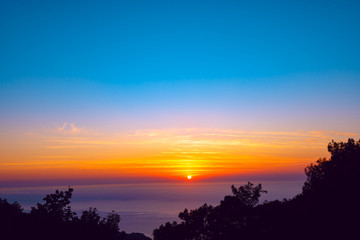 Orange sun sets on the horizon over the purple sea