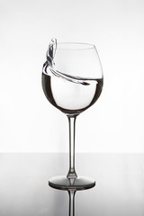 Transparent wine glass with frozen splash of water. The glass stands on a black mirror surface on which its reflection is visible. The background is white.