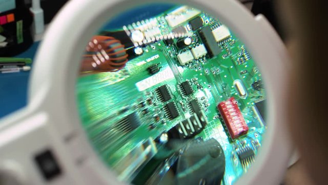Precision quality control checks by worker on printed circuit board with magnifying glass. PCB