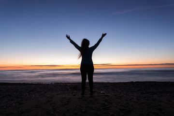 Fototapeta na wymiar Freedom, holiday and victory concept - Silhouette of woman with hands up while standing on the sea beach at sunset