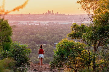 Girl watches sunset over the Perth City skyline from the Perth hills (Kalamunda Zig Zag). Perth, Western Australia, Australia. - obrazy, fototapety, plakaty