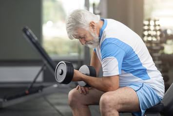 Fototapeta na wymiar Fit elderly man working out with dumbbells in gym.
