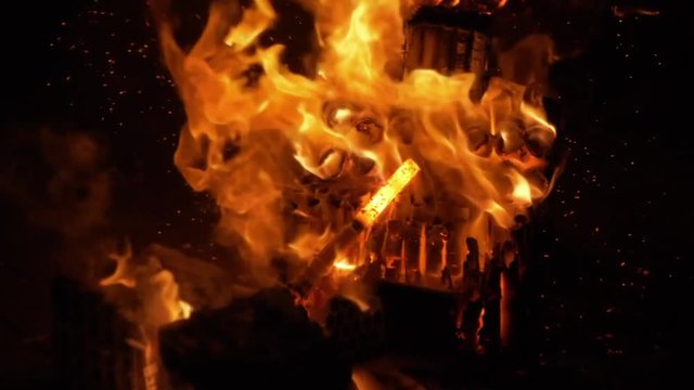 A slowmotion shot of trowing a bottle of beer true a big street fire with big flames dancing in the night wind.