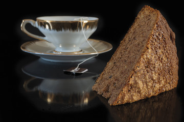 tazza da te con bustina te e fetta torta al cacao e noci fondo nero