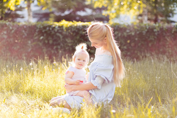 Portrait of happy young mother with little cute baby daughter spending time together in summer park looking at camera. Happiness, happy parenting and childhood concept