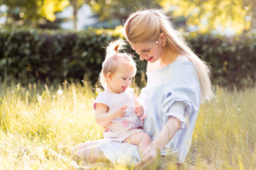 Obraz premium Young beautiful blonde mother with her baby girl laughing together and playing in green park outdoors at sunny day