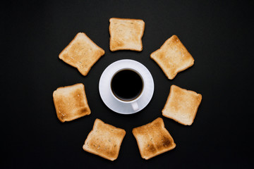 White cup with coffee and Toast piled around on a dark background. Flat lay, top view