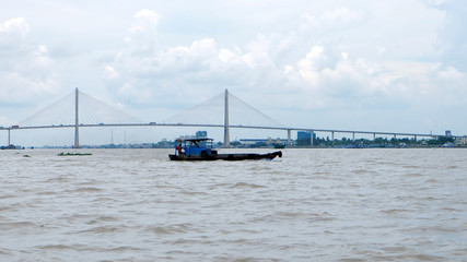 A boat crossing Mekong River, Vietnam, with a bridge in the background.