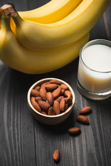 Almond milk in a glass with almond nuts and bananas on a wooden table. Healthy food and drink concept.