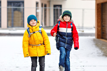 Two little kids boys of elementary class walking to school during snowfall. Happy children having...