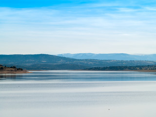Obraz premium Landscape of a reservoir and mountains in a day with fog and clouds and birds swimming and flying in in La Maya Reservoir (Salamanca)