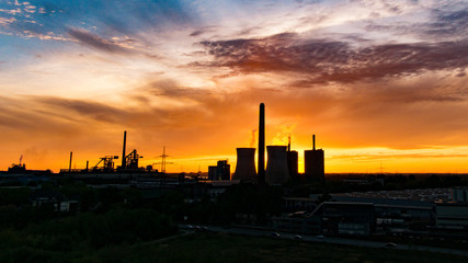 Fototapeta na wymiar Industrie im Sonnenuntergang am Sommerabend mit Schornsteinen und Dampf am Sommerabend in Duisburg, Deutschland