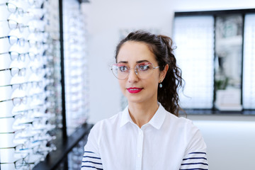 Close up of Caucasian woman with curly hair wearing glasses while standing at optician.